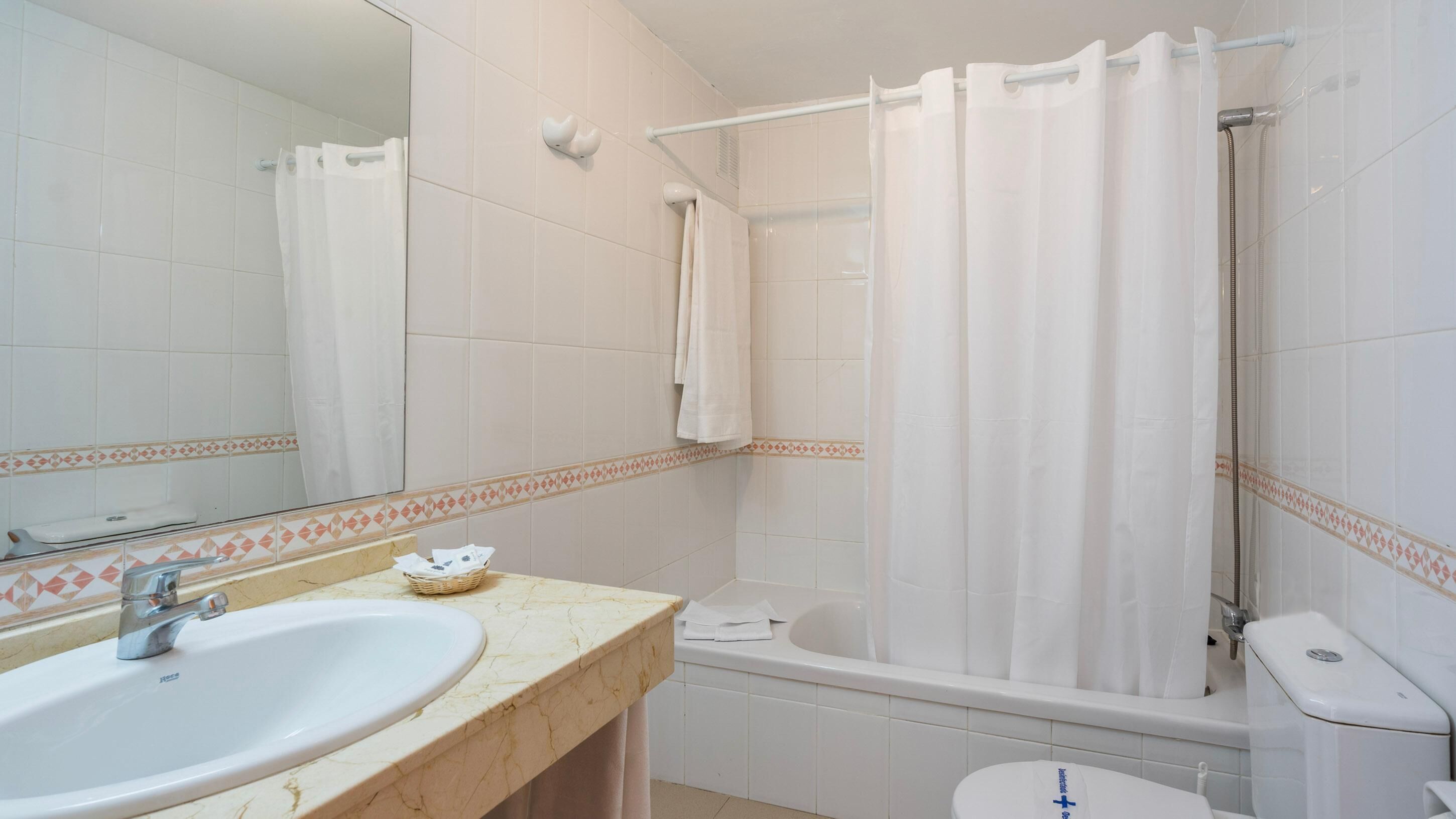 A bathroom with a sink, mirror, bathtub, and toilet.