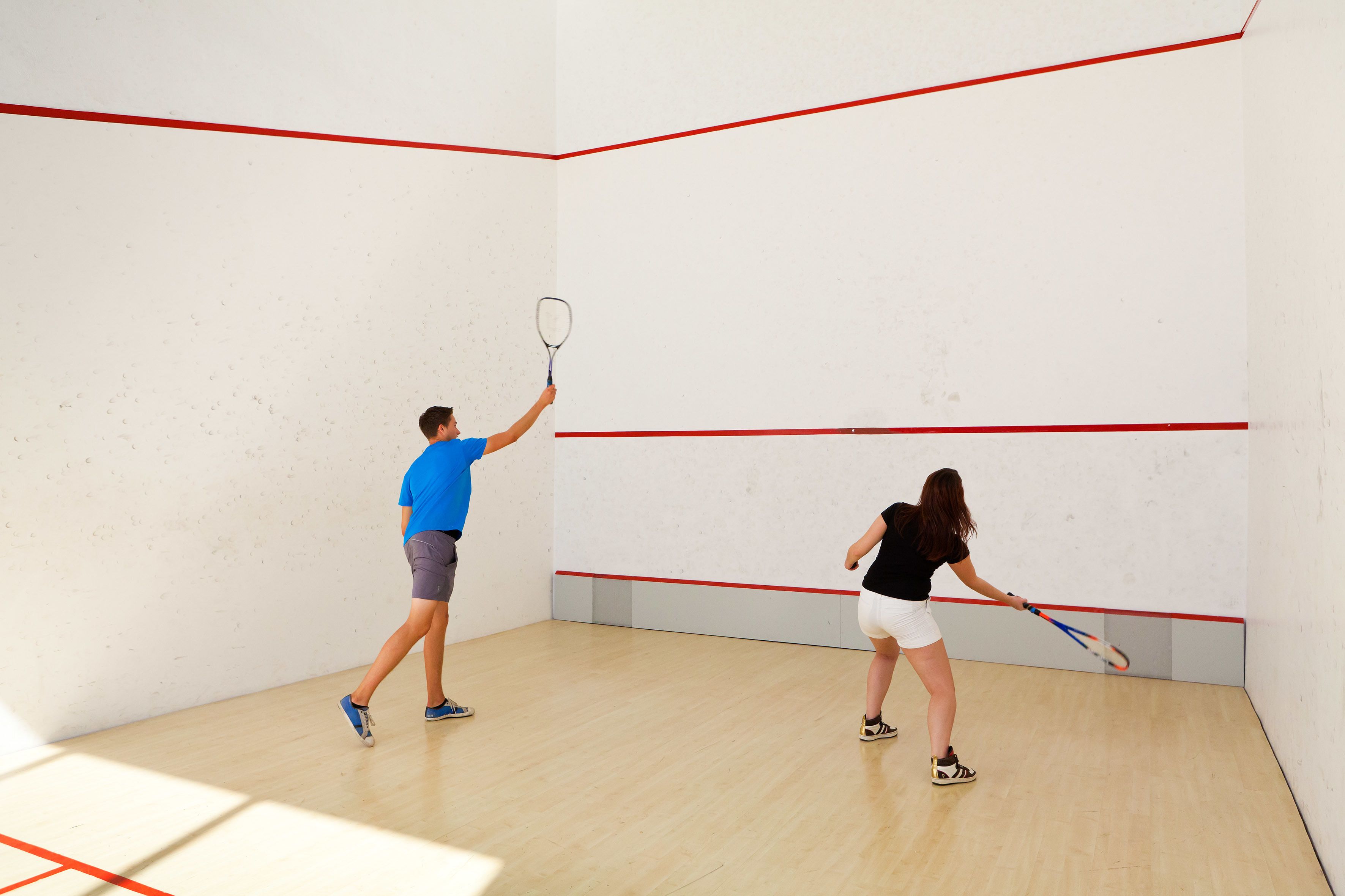 Uma quadra de squash com piso de madeira e linhas divisórias vermelhas.
