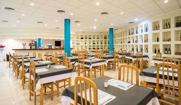 A restaurant with multiple tables and chairs, a counter with a menu, and shelves with bottles. - BLUESEA Costa Teguise Gardens (Teguise)