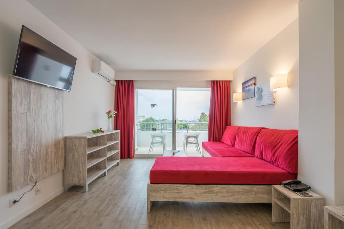Une chambre moderne avec un canapé rouge, un téléviseur fixé au mur, un meuble en bois et un balcon avec vue.