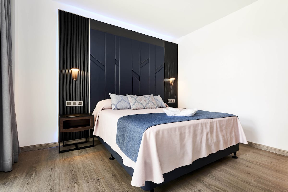 Une chambre à coucher moderne avec un lit, une tête de lit sombre, des lampes de chevet et un plancher en bois.
