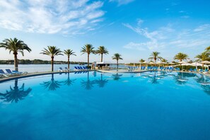 A swimming pool with blue water, surrounded by palm trees and lounge chairs. - Hotel BelleVue Club (Alcúdia)