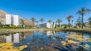 A large, modern hotel with multiple floors, a central courtyard with a fountain, and surrounding palm trees. - Hotel BelleVue Club (Alcúdia)