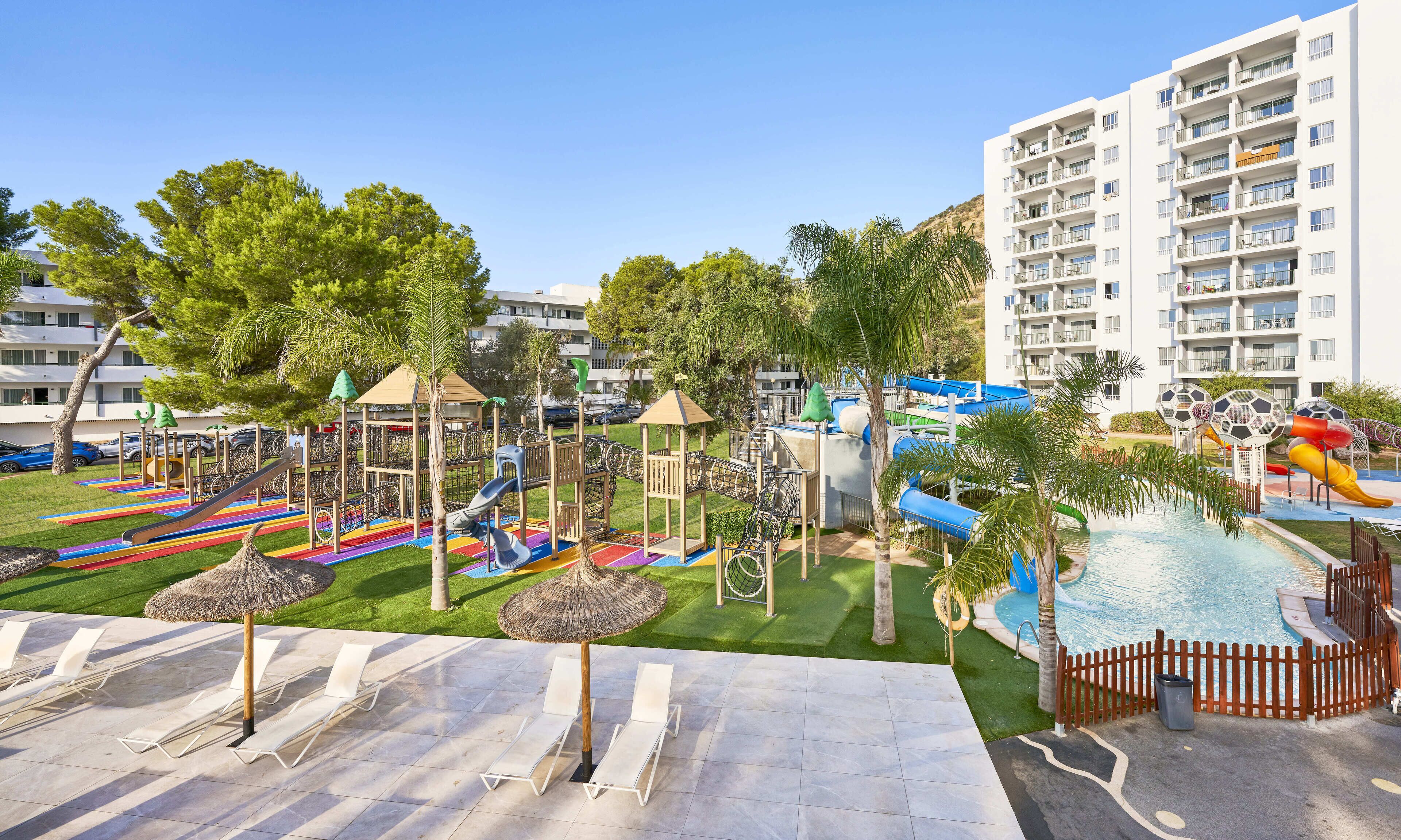 A hotel with a children's play area, a swimming pool, and a beach with lounge chairs.