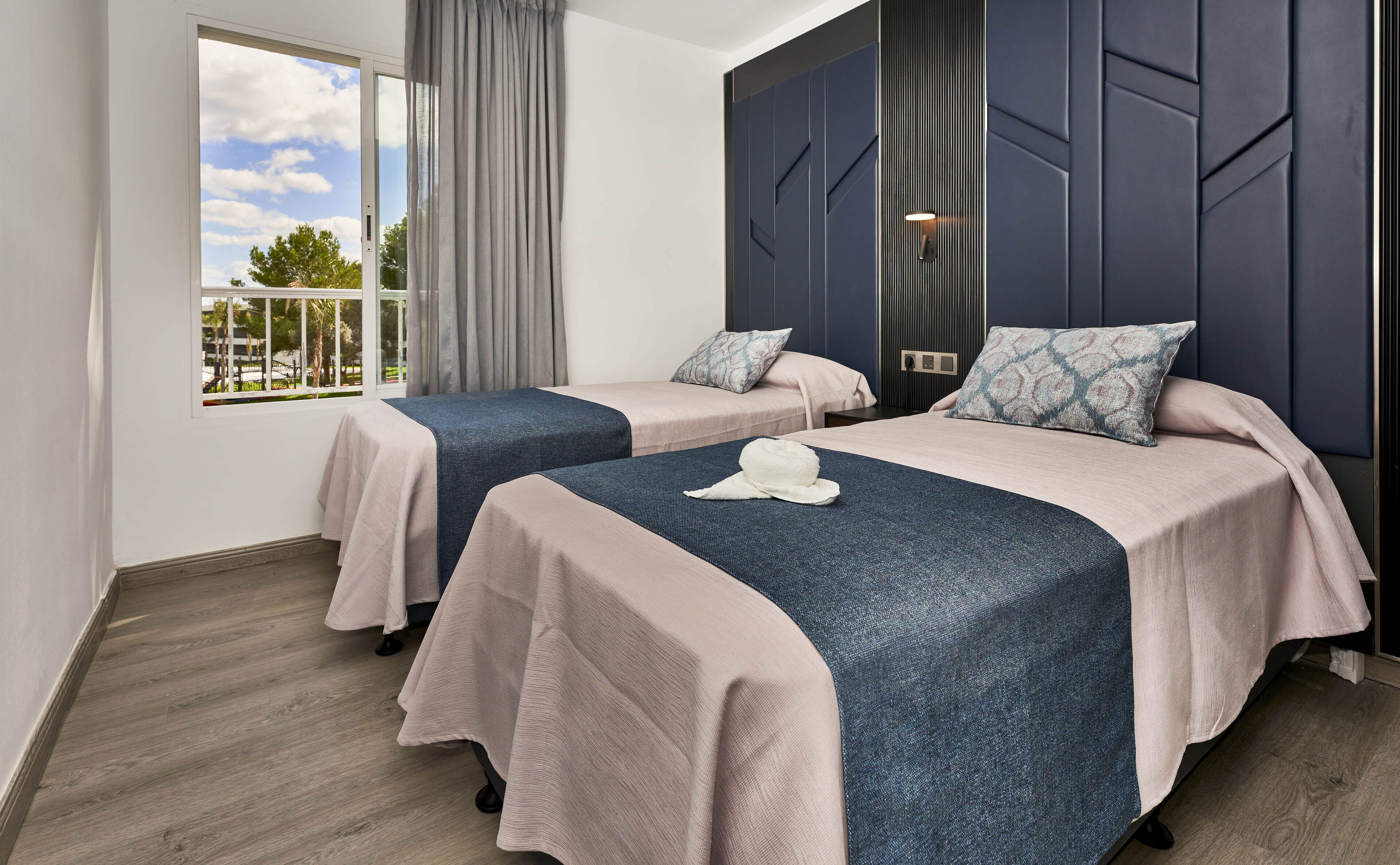 A hotel room with two beds, a large window, and a view of the outdoors.