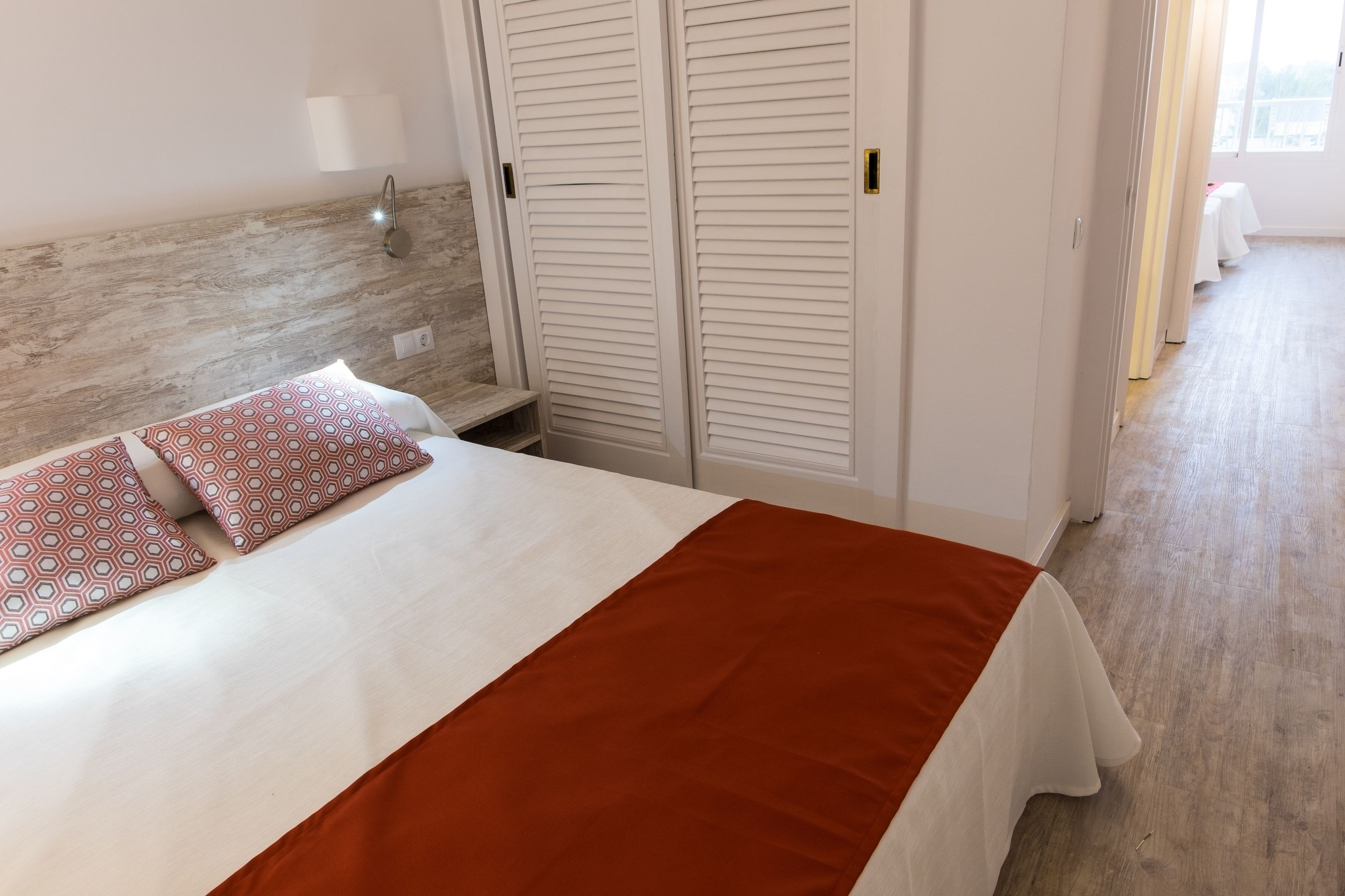 Una cama bien tendida con almohadones estampados, un cabecero de madera y una mesita de noche blanca.