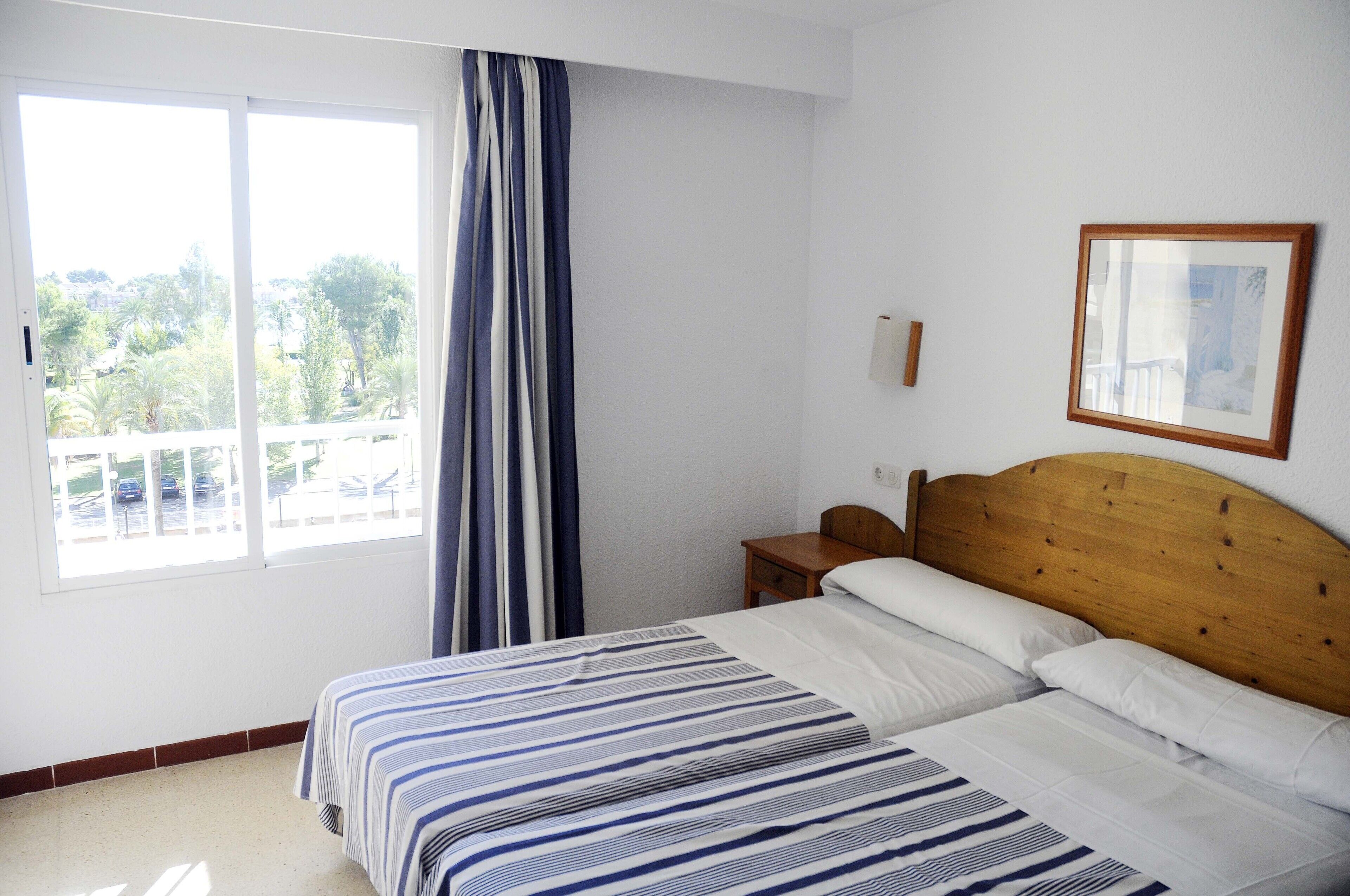 Un dormitorio con una cama grande, cabecera de madera, mesita de noche, ventana con cortinas e imagen enmarcada en la pared.