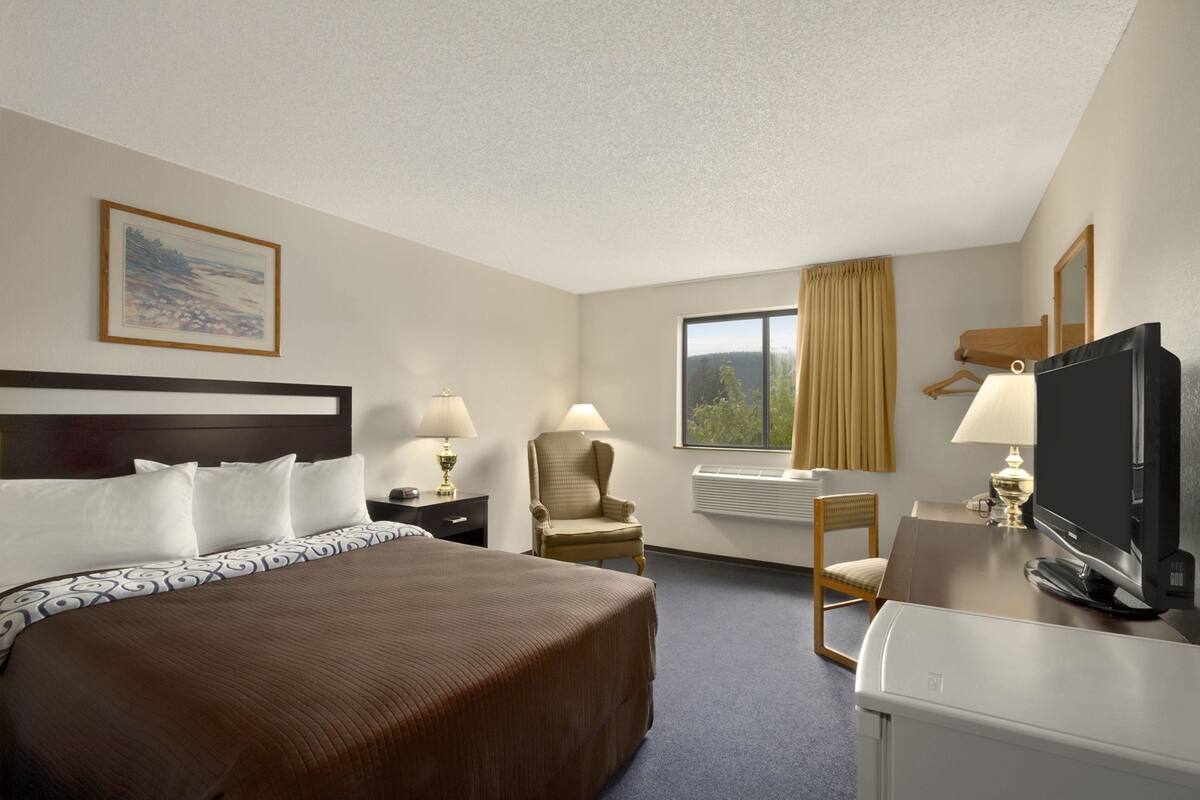 A hotel room with a large bed, a desk with a television, a chair, and a window with curtains.