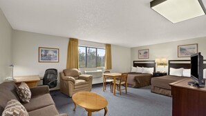 Habitación de hotel con sofá, sillón, mesa de comedor y televisor sobre un escritorio.