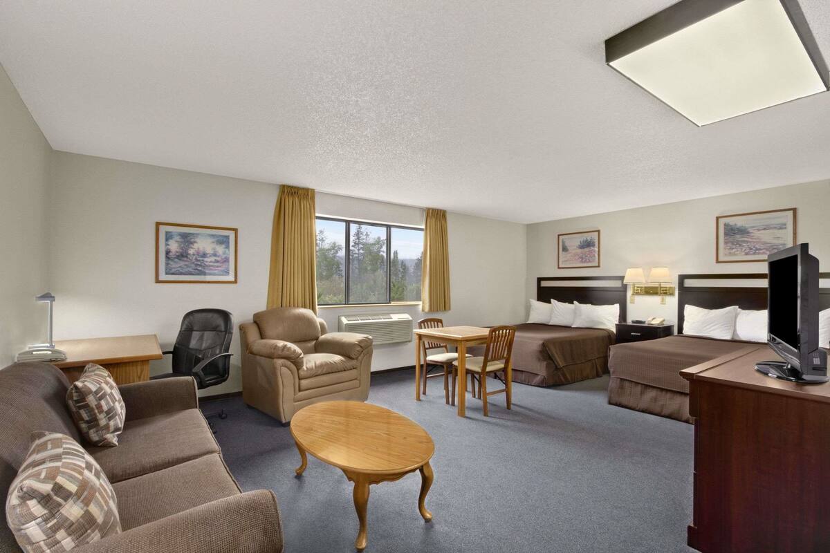 A hotel room with a sofa, armchair, dining table, and a TV on a desk.