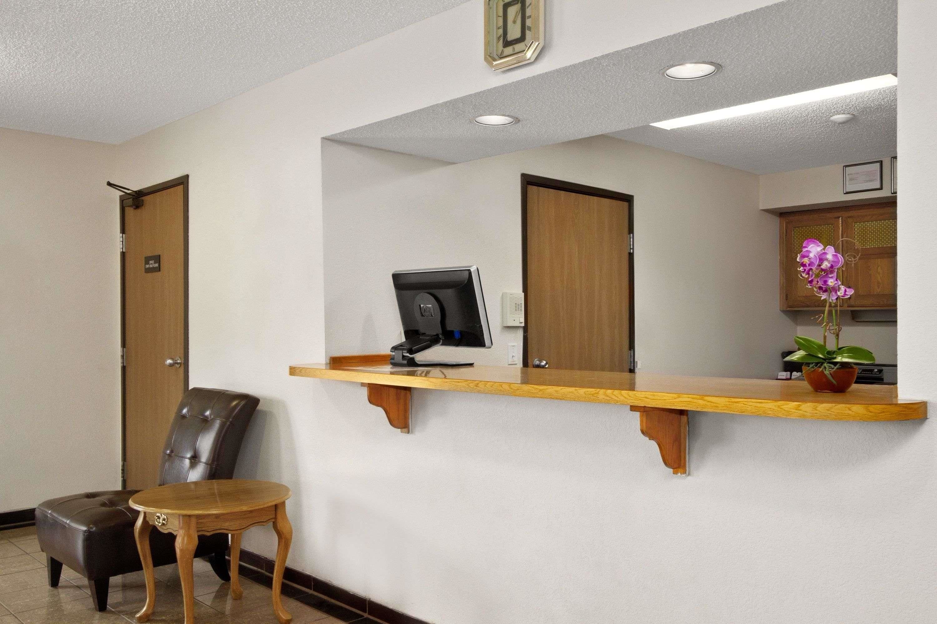 A reception area with a wooden counter, a computer monitor, a chair, and a small table.