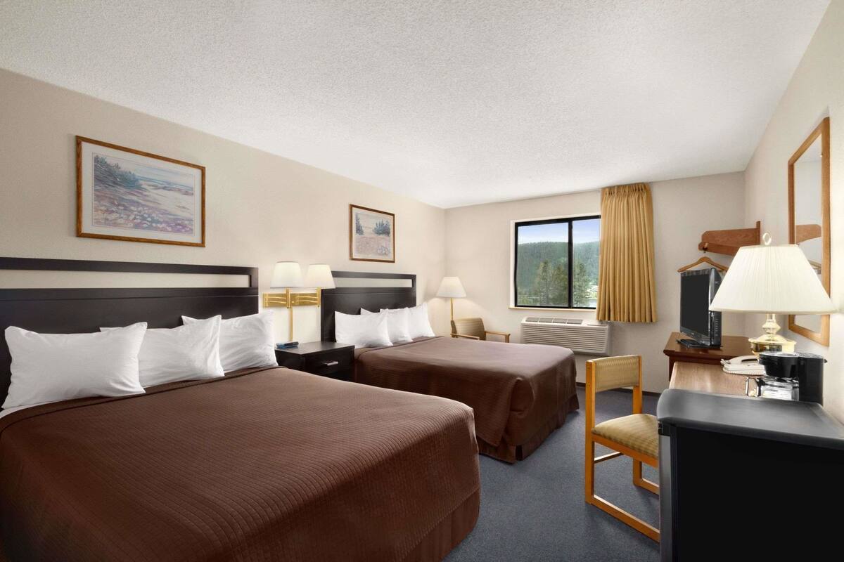 A hotel room with two beds, a desk, a chair, a TV, and a window with curtains.