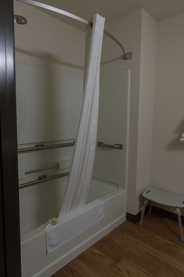Un área de ducha con puerta de vidrio, cortina blanca y un pequeño banco blanco.