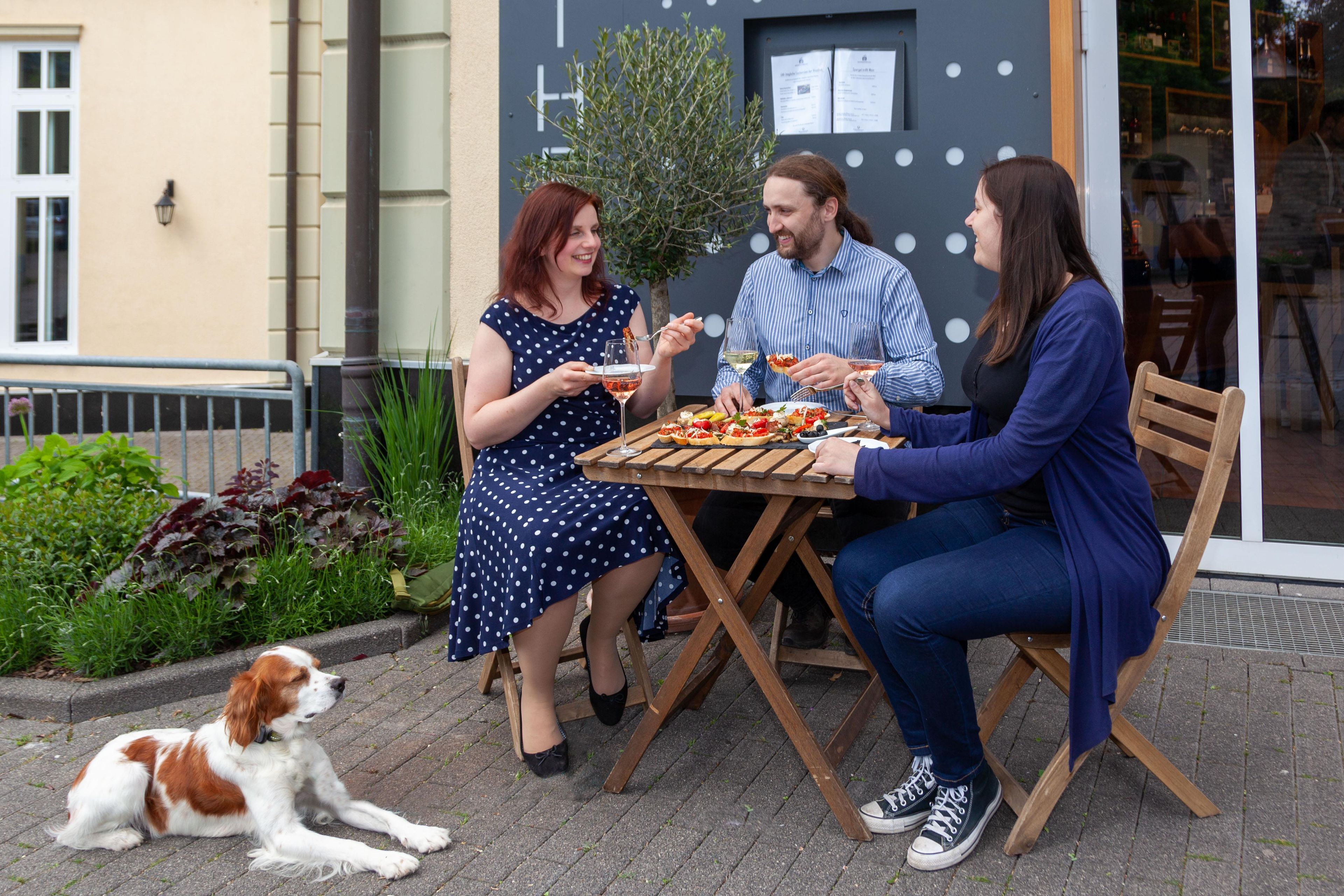 Three people dining outdoors at a wooden table with a variety of dishes.
