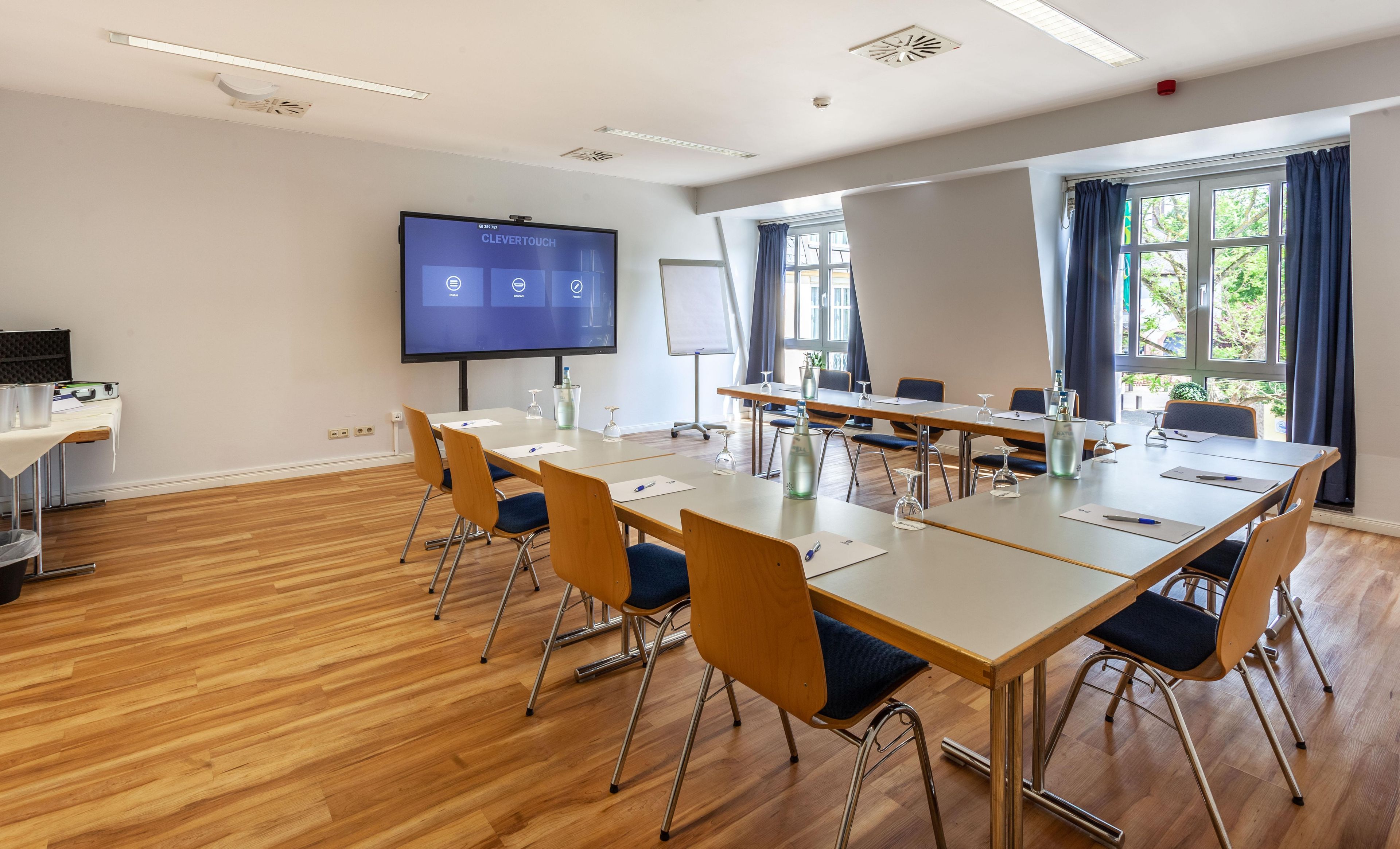Ein Konferenzraum mit einer großen Leinwand, Holztischen und Stühlen.