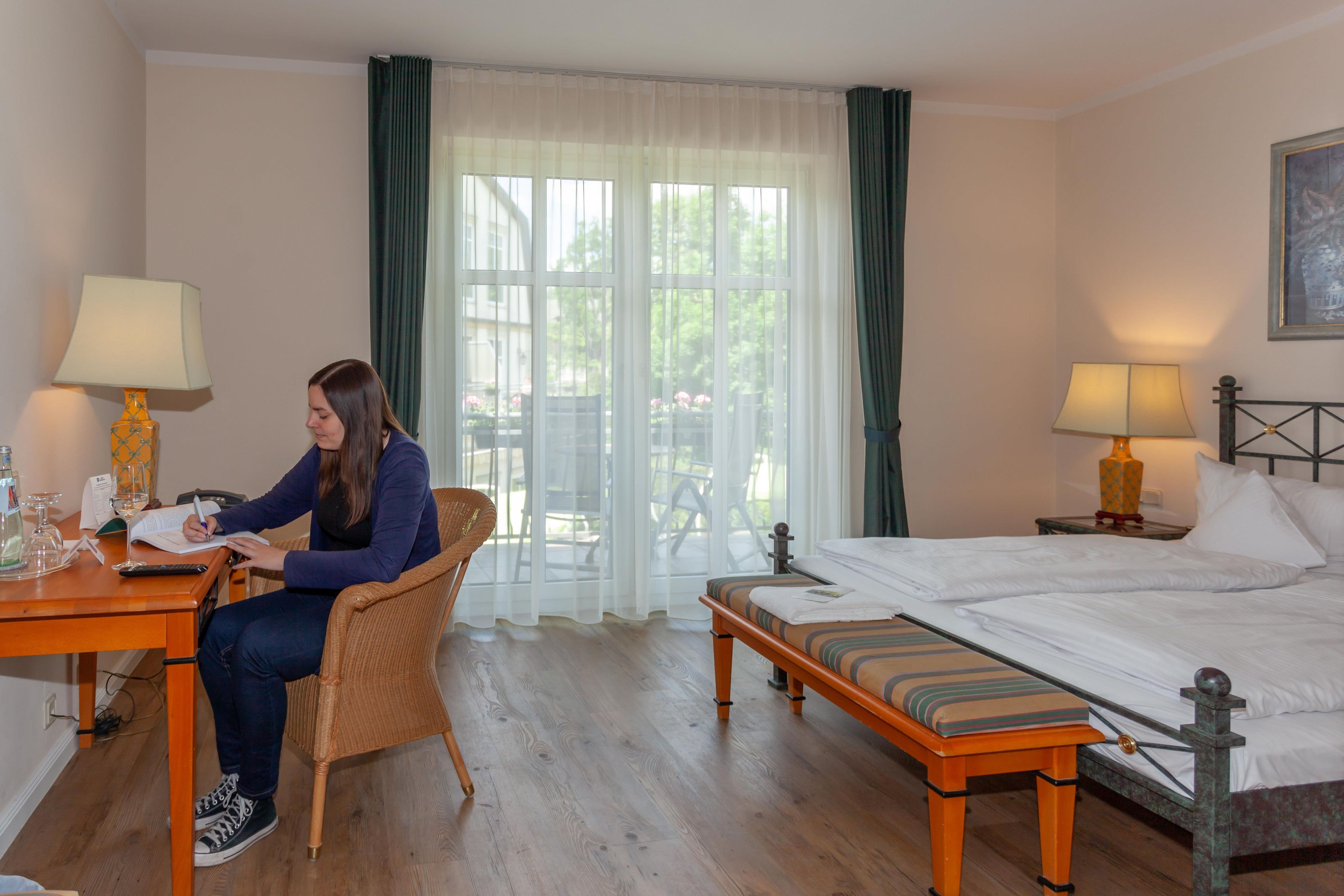 Ett hotellrum med en säng, ett skrivbord med en lampa, en stol och ett fönster med gardiner.