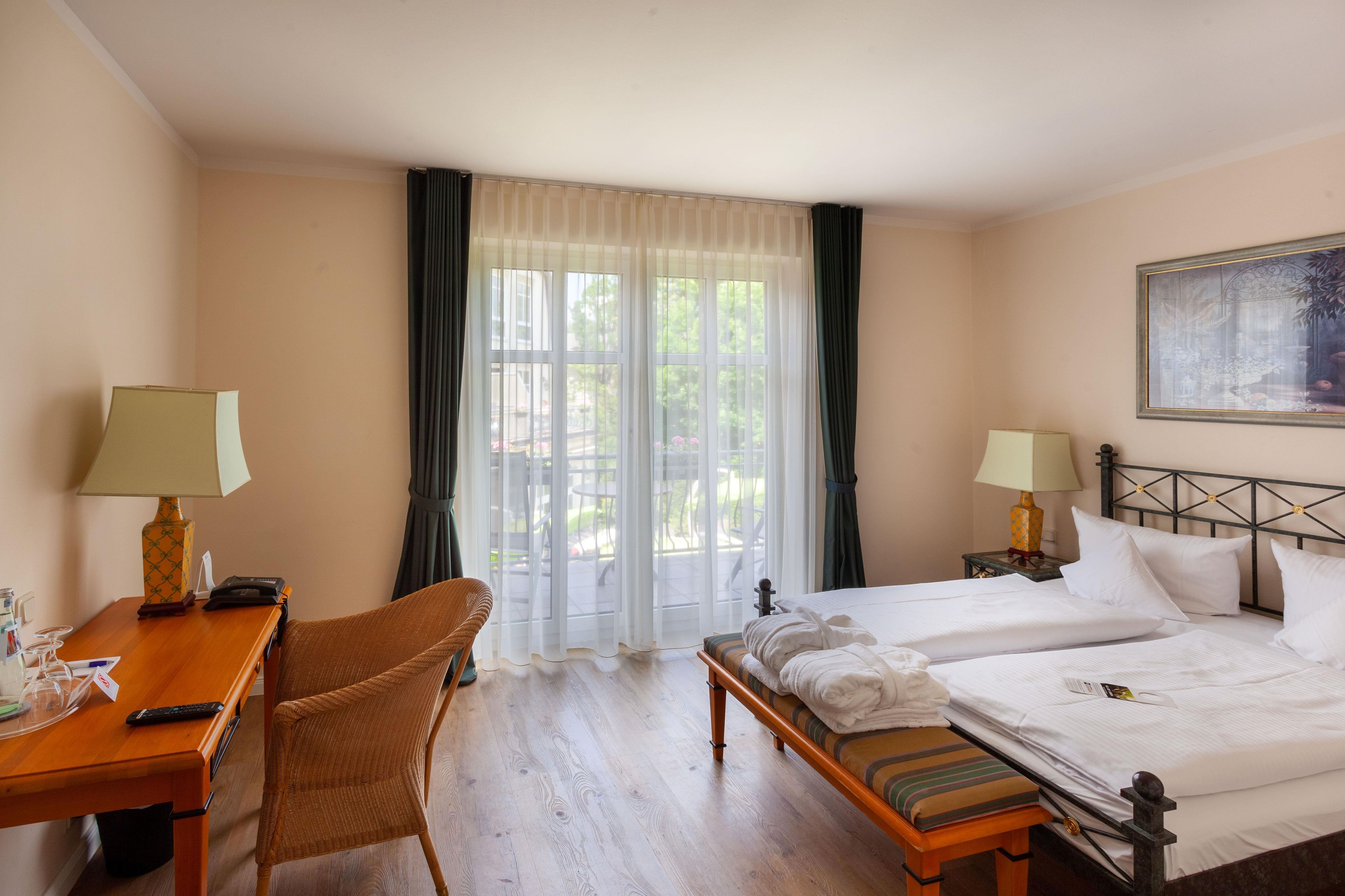 Una habitación de hotel con cama, dos mesitas de noche, un escritorio, una silla y una ventana con cortinas.