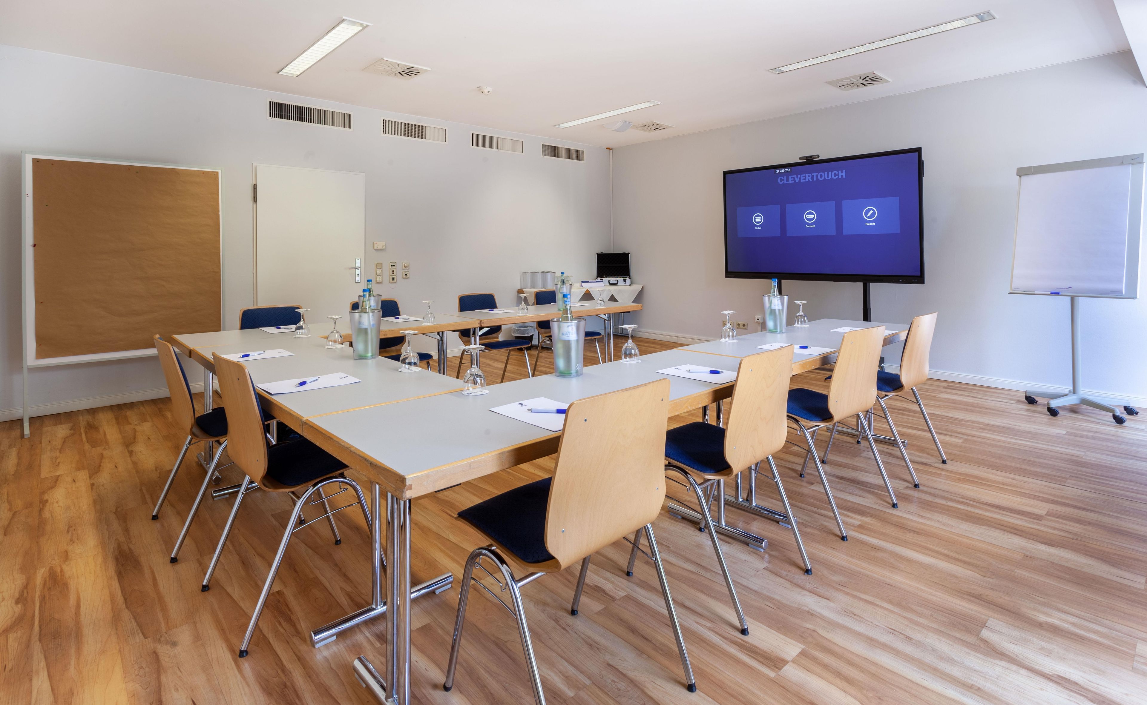 A conference room with a large screen displaying 'CleverTouch' software, wooden tables, chairs, and a whiteboard.