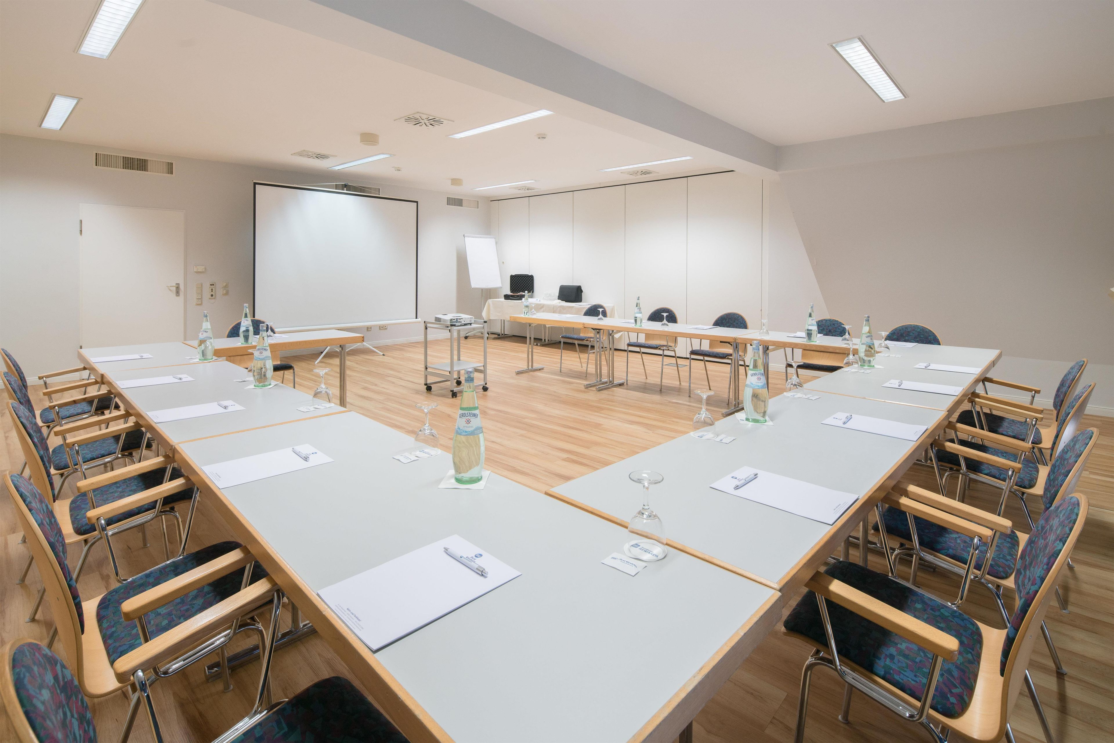 A conference room with a long table, chairs, a projector screen, and a whiteboard.