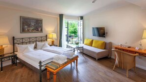 Une chambre d’hôtel avec deux lits, un canapé, un bureau, une télévision et un balcon donnant sur un espace verdoyant.