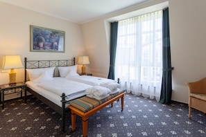 Quarto de hotel com duas camas, um banco, um quadro e uma janela com cortinas.