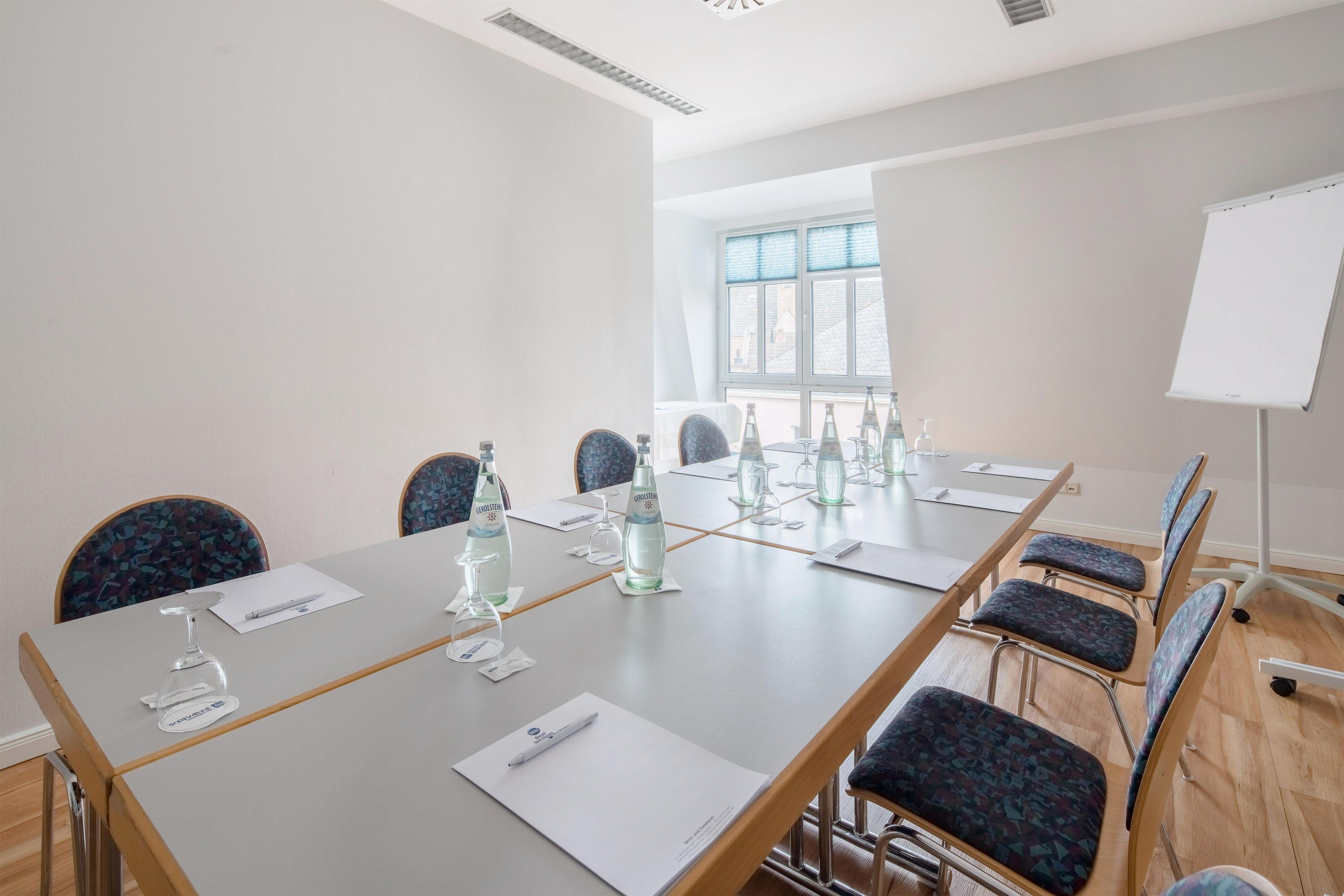 Ein Konferenzraum mit einem langen Tisch, Stühlen, Wasserflaschen und Dokumenten.