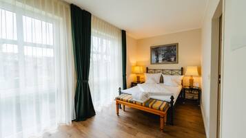 Ein Hotelzimmer mit Bett, Nachttischlampen, einem Gemälde und Blick durch transparente Vorhänge.