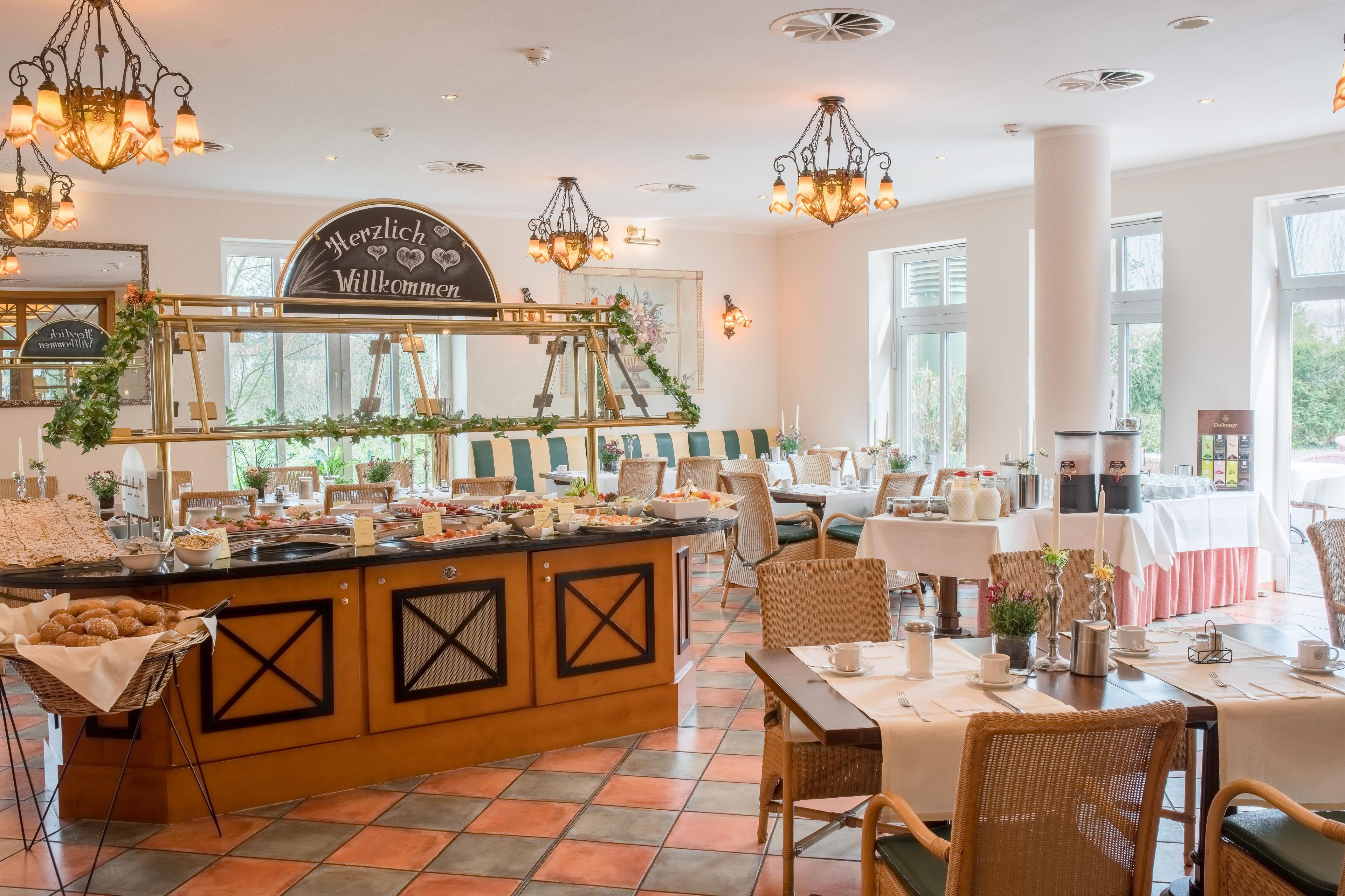 A buffet area with a variety of food items, a sign reading 'Herzlich Willkommen,' and a seating area with tables and chairs.