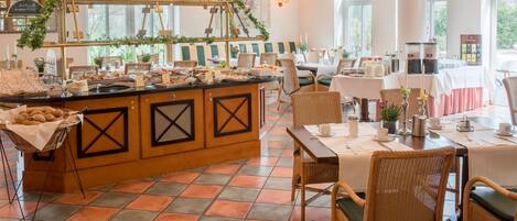 A buffet area with a variety of food items, a sign reading 'Herzlich Willkommen,' and a seating area with tables and chairs.