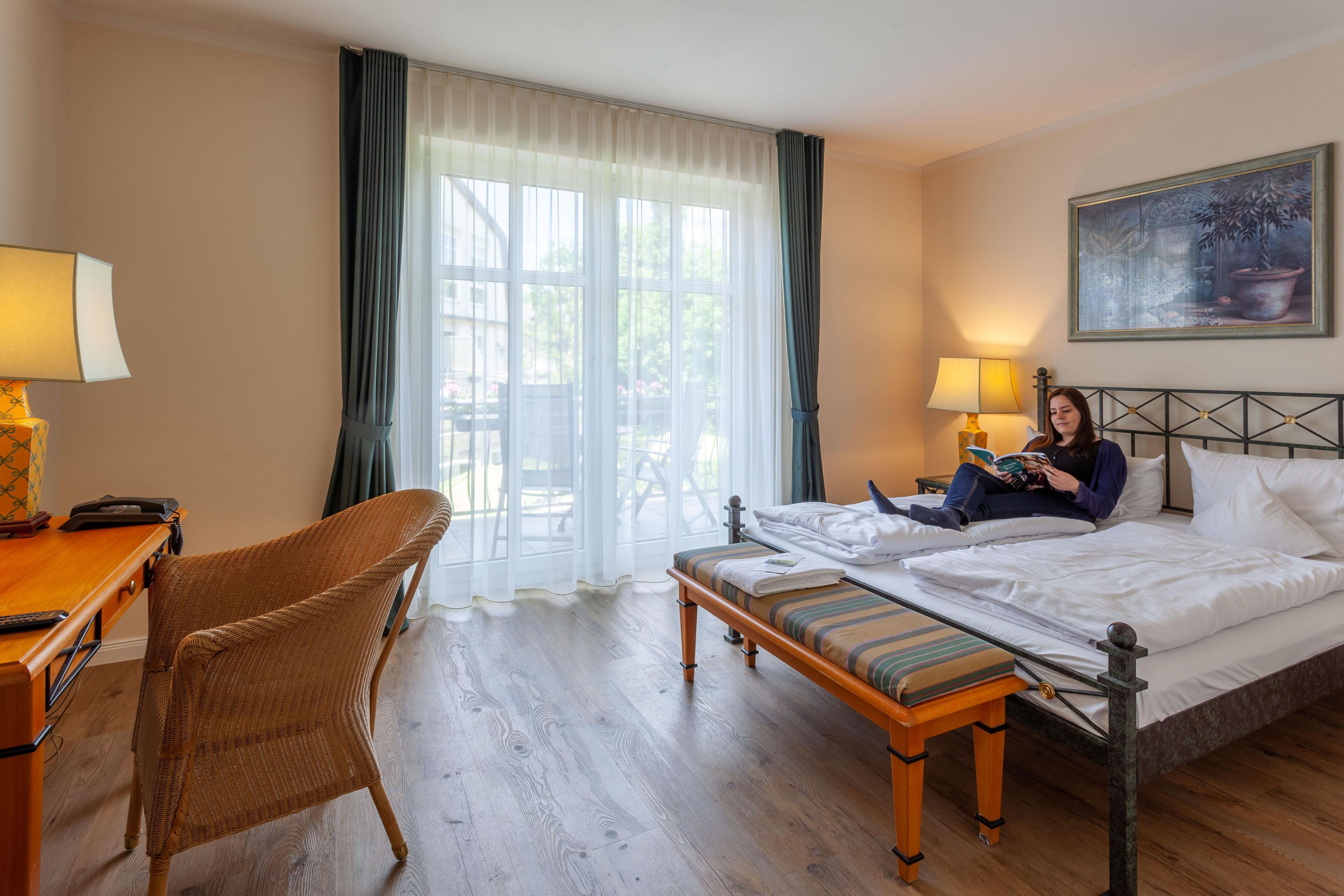 Una habitación de hotel con una cama, una silla, un escritorio con lámpara y un cuadro en la pared.