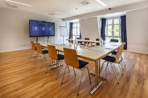 Uma sala de conferências com uma mesa grande, cadeiras, tela de projetor e quadro branco.