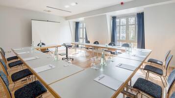 Ein Konferenzraum mit langen Tischen, Stühlen und einer Projektionsleinwand.
