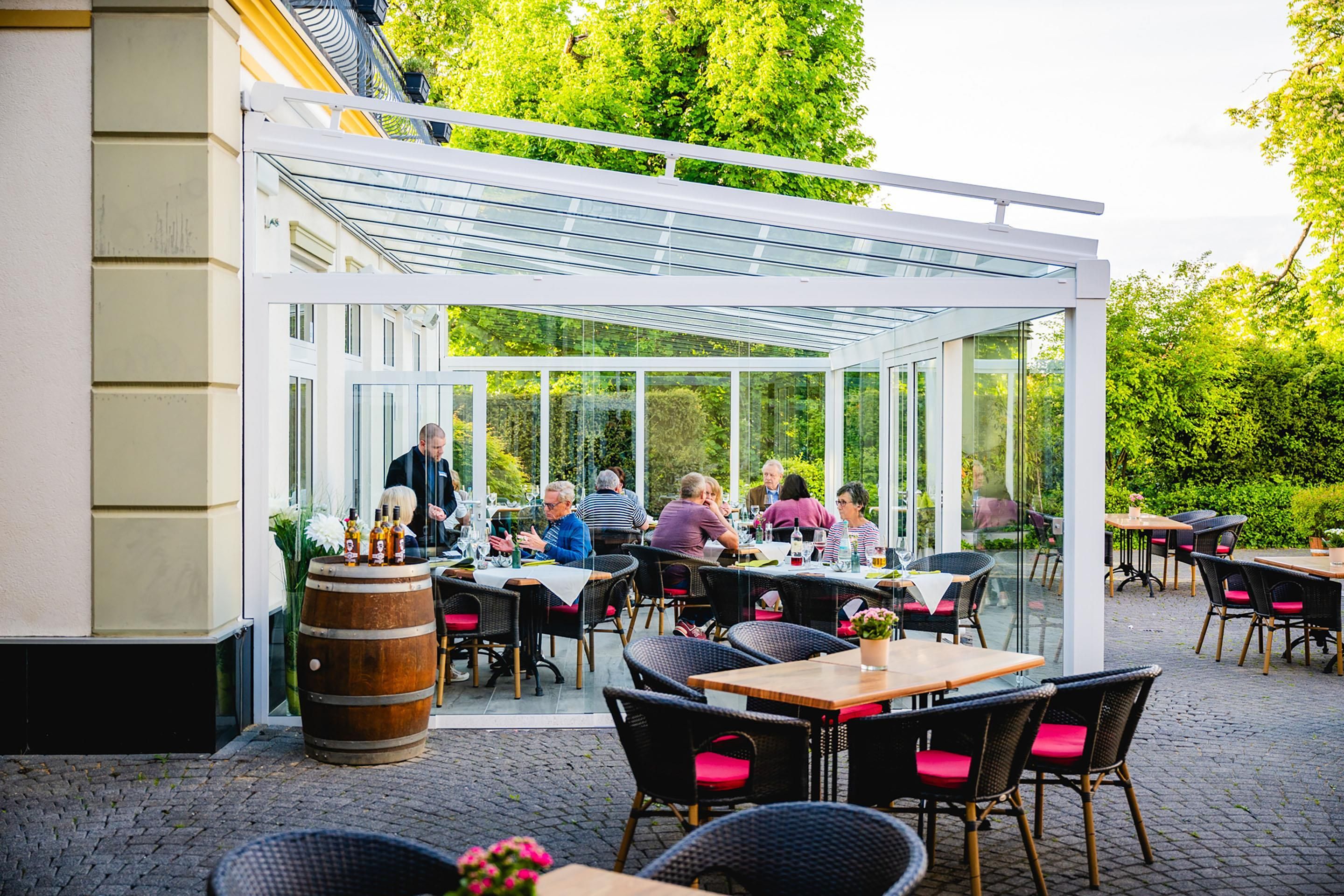 Eine Terrasse im Freien mit Tischen und Stühlen, einer Glaskonstruktion und einem Fass.