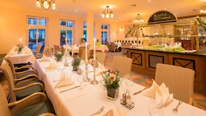 Un restaurant où les tables sont dressées pour le service, avec des chaises en osier et des nappes blanches.