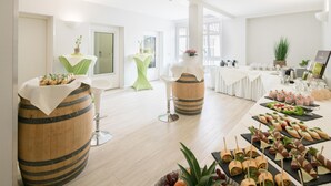 Een ruime kamer met een lange tafel waarop verschillende soorten eten staan, en enkele decoratieve tafels met planten.