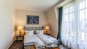 Een hotelkamer met een bed, twee bedlampen, een schilderij aan de muur en een raam met gordijnen.