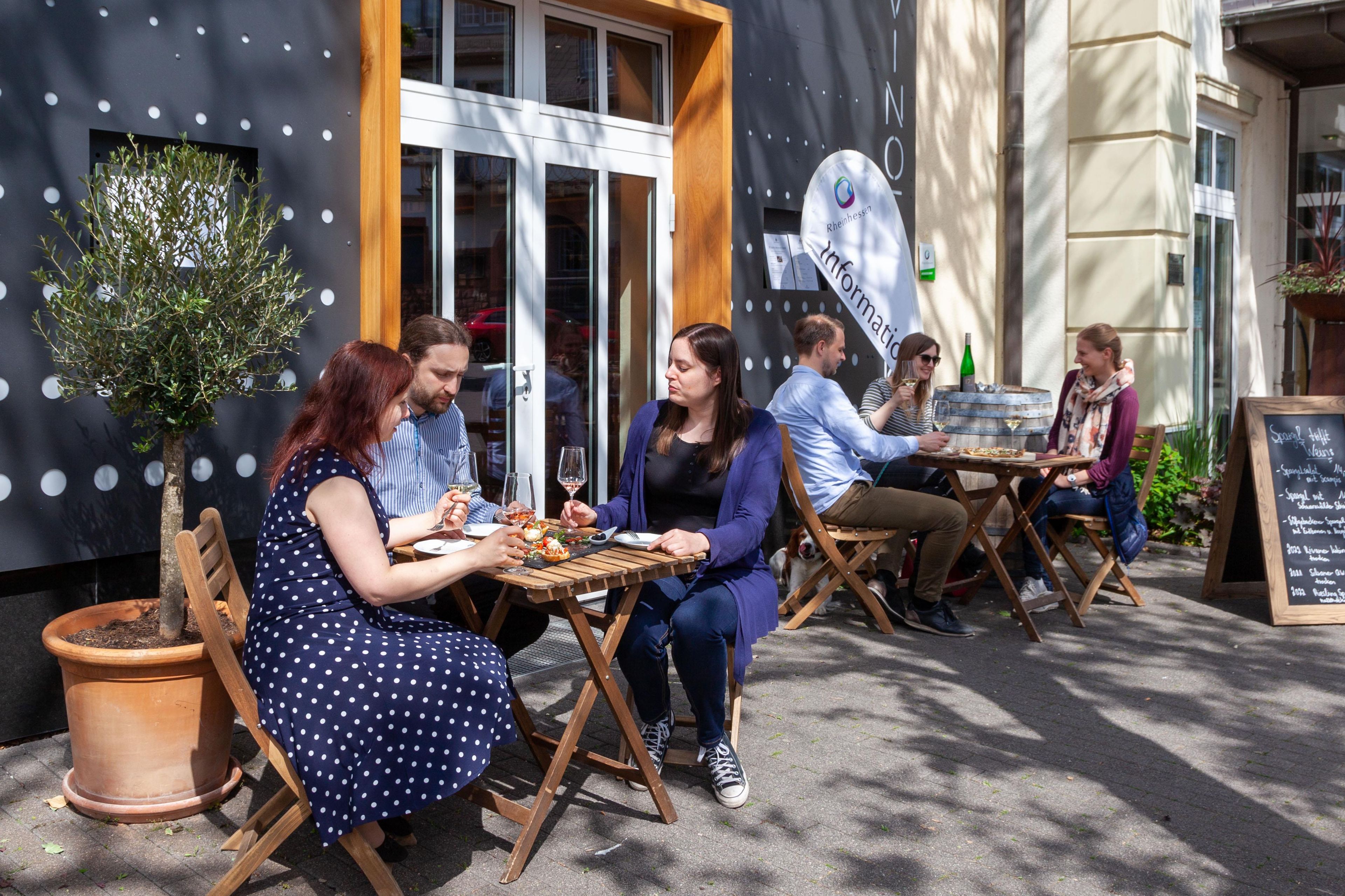 An outdoor seating area with tables and chairs, a potted plant, and a sign with text.
