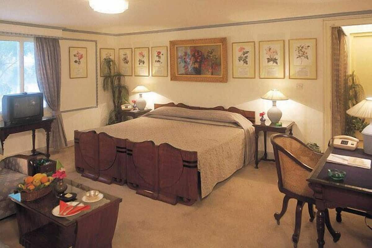 Una habitación de hotel con una cama grande, dos mesitas de noche con lámparas, un escritorio con una silla y un televisor sobre un mueble.
