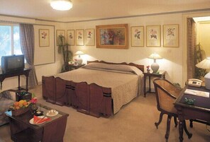 Una habitación de hotel con una cama grande, dos mesitas de noche con lámparas, un escritorio con una silla y un televisor sobre un mueble.