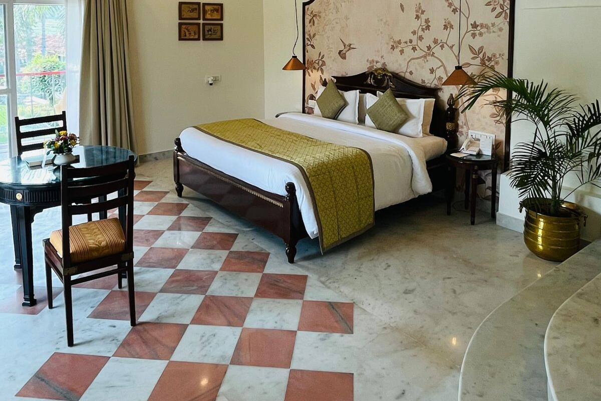 Una habitación de hotel con cama, escritorio, silla, ventilador de techo y una planta en maceta.
