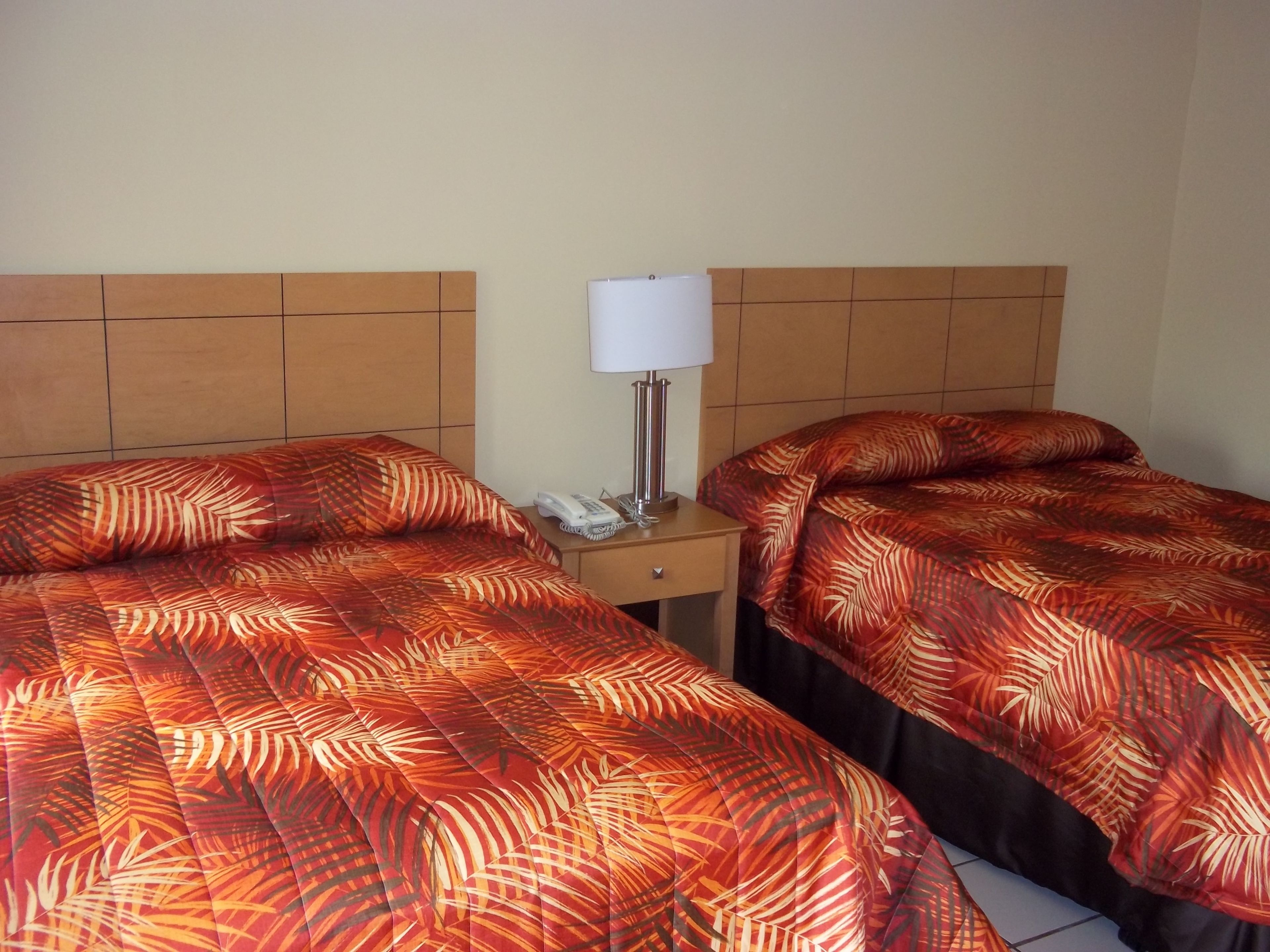 Une chambre d’hôtel avec deux lits, chacun recouvert d’une couvre-lit aux motifs de feuilles rouges et oranges. Une table de chevet avec une lampe et un téléphone se trouve entre les deux lits.