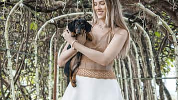 A woman holding a dog on a bridge with a natural, vine-covered archway.