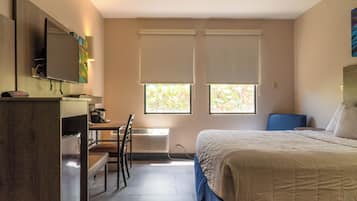 Una habitación de hotel con una cama, un escritorio con silla, un televisor y dos ventanas con persianas.