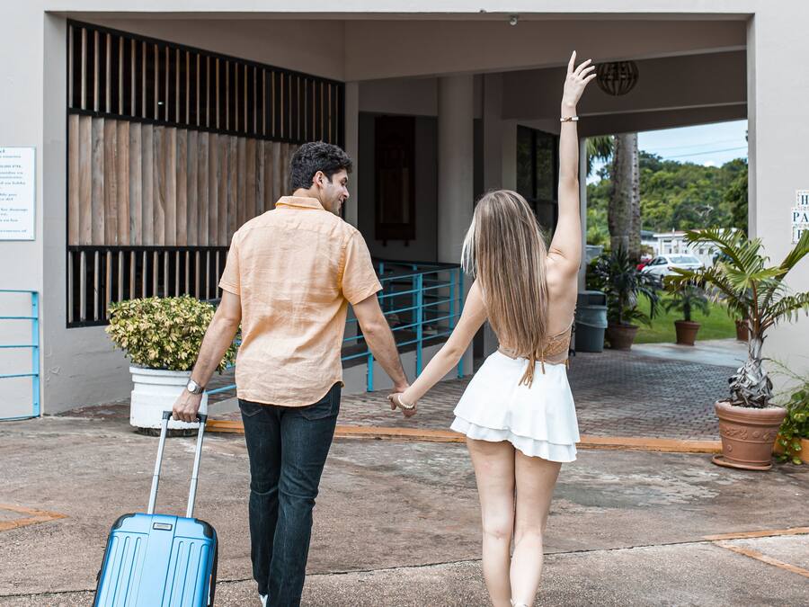 Um casal de mãos dadas caminhando em direção a um prédio com uma placa que diz 'Hotel el FARO'.