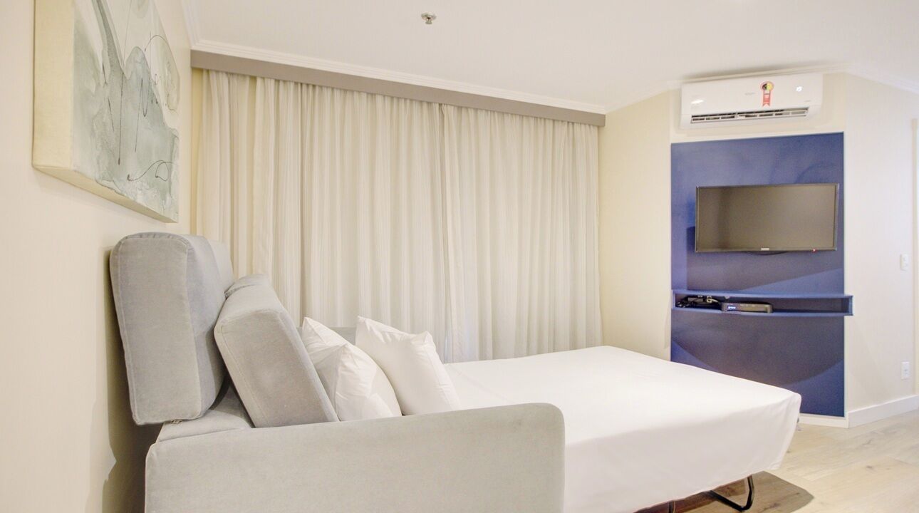 A modern hotel room with a white sofa, a flat-screen TV, and a built-in air conditioning unit.