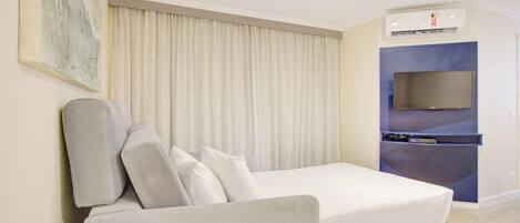 A modern hotel room with a white sofa, a flat-screen TV, and a built-in air conditioning unit.