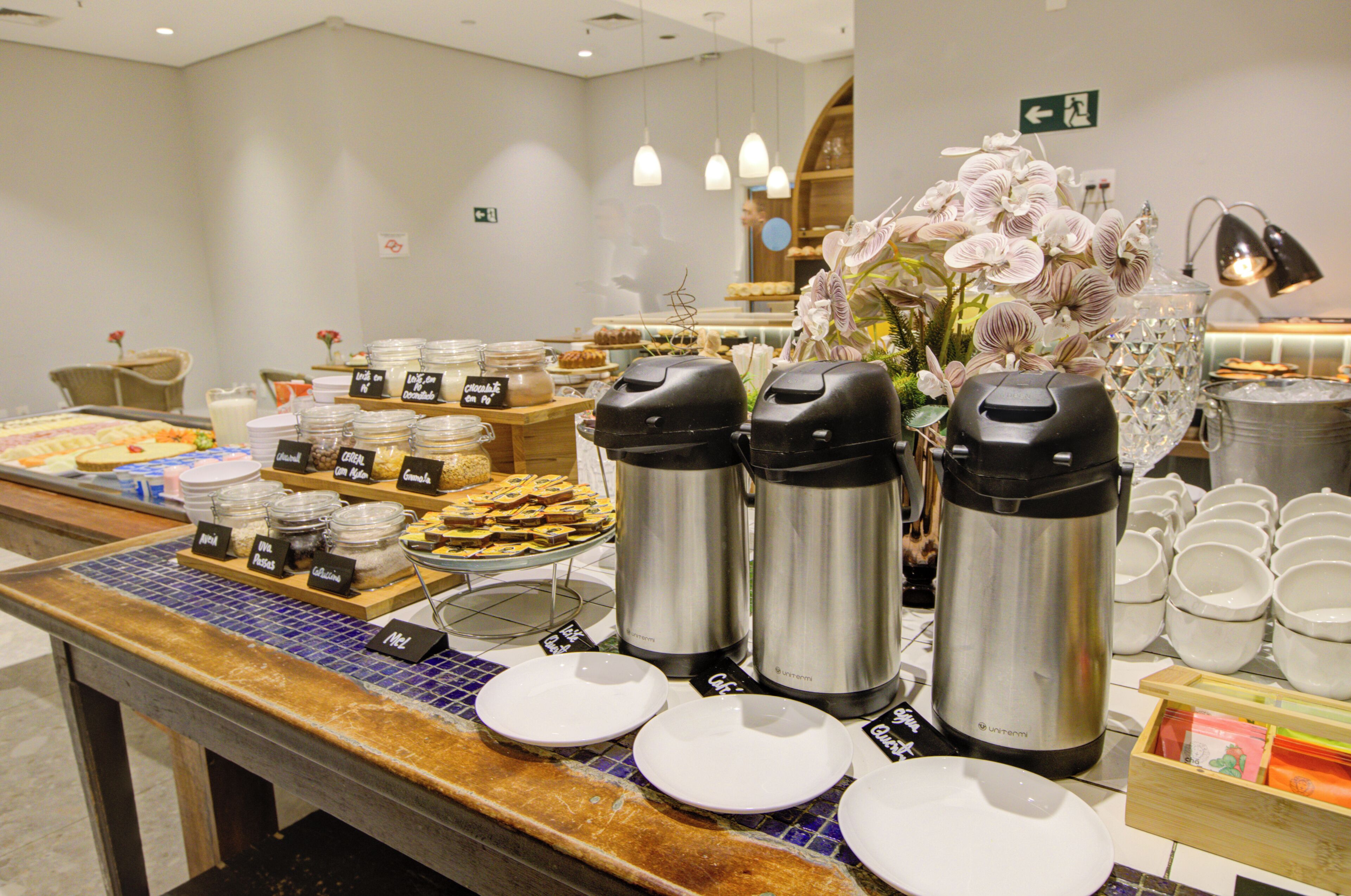 Zona de bufé con diversos alimentos, cafeteras y un arreglo floral.