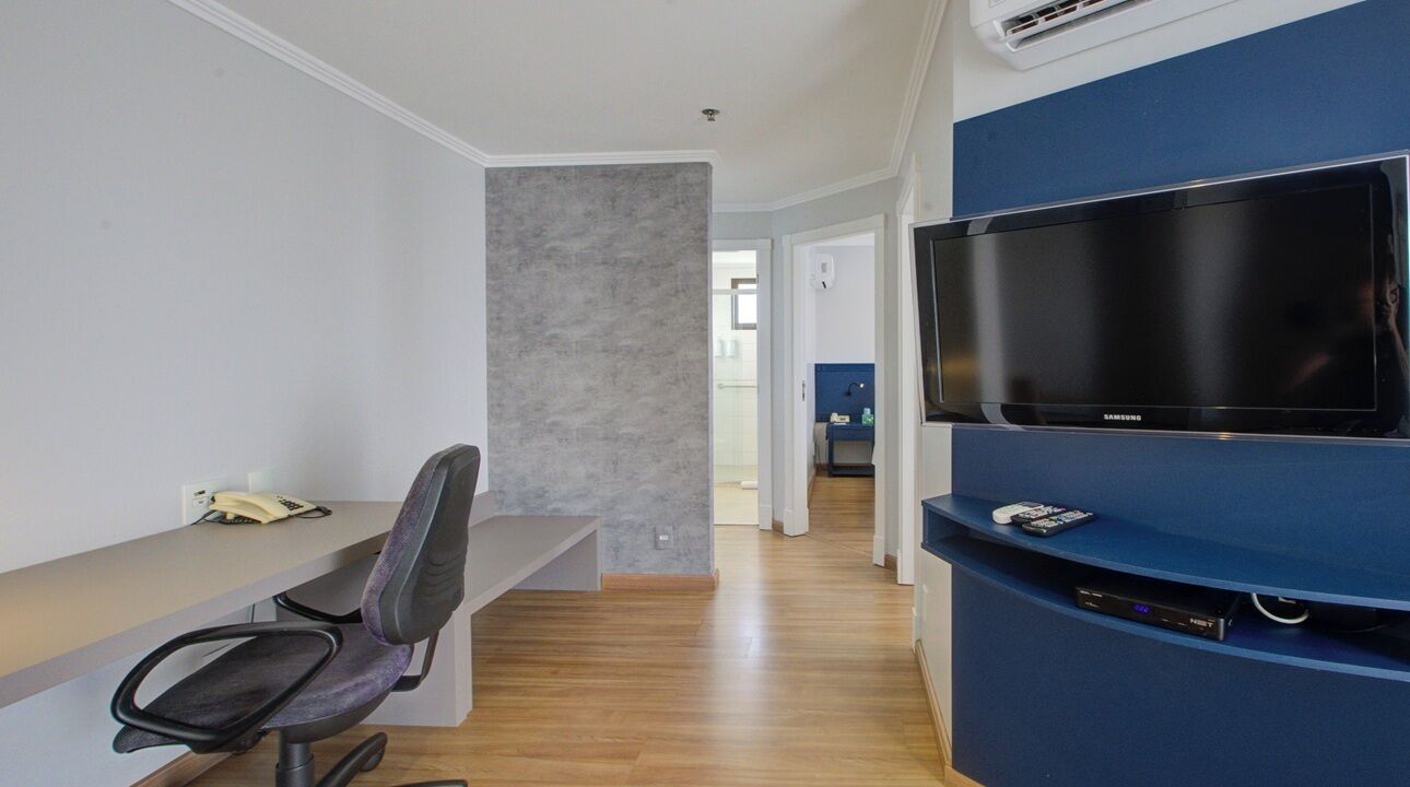 A modern office space with a desk, chair, and a mounted flat-screen TV.