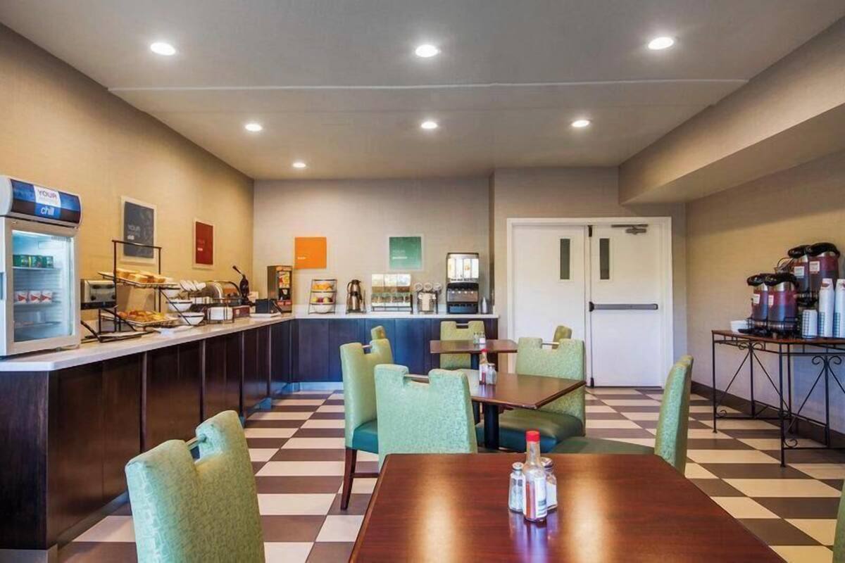 A hotel room with a checkered floor, a kitchenette, a seating area with chairs, and a counter with a coffee machine.