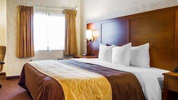 A hotel room with a large bed, a wooden headboard, a nightstand with a lamp, and a window with curtains.